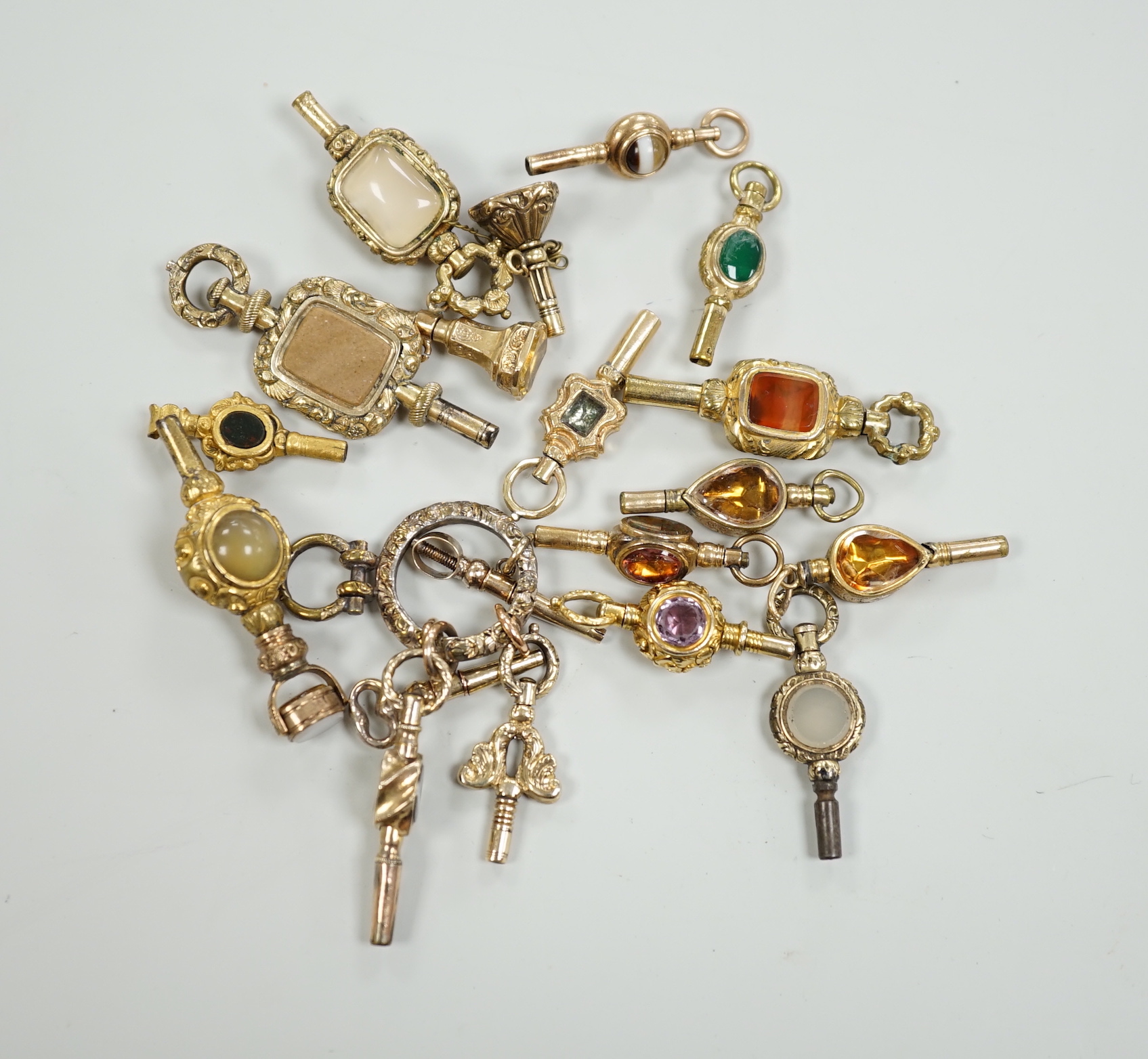 Sixteen assorted 19th century yellow metal overlaid and mainly gem set small watch keys, including chalcedony, citrine, amethyst, banded agate, bloodstone and a ring with four keys attached, largest 47mm.